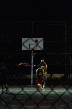 Two men playing basketball at night on an outdoor court in Istanbul.