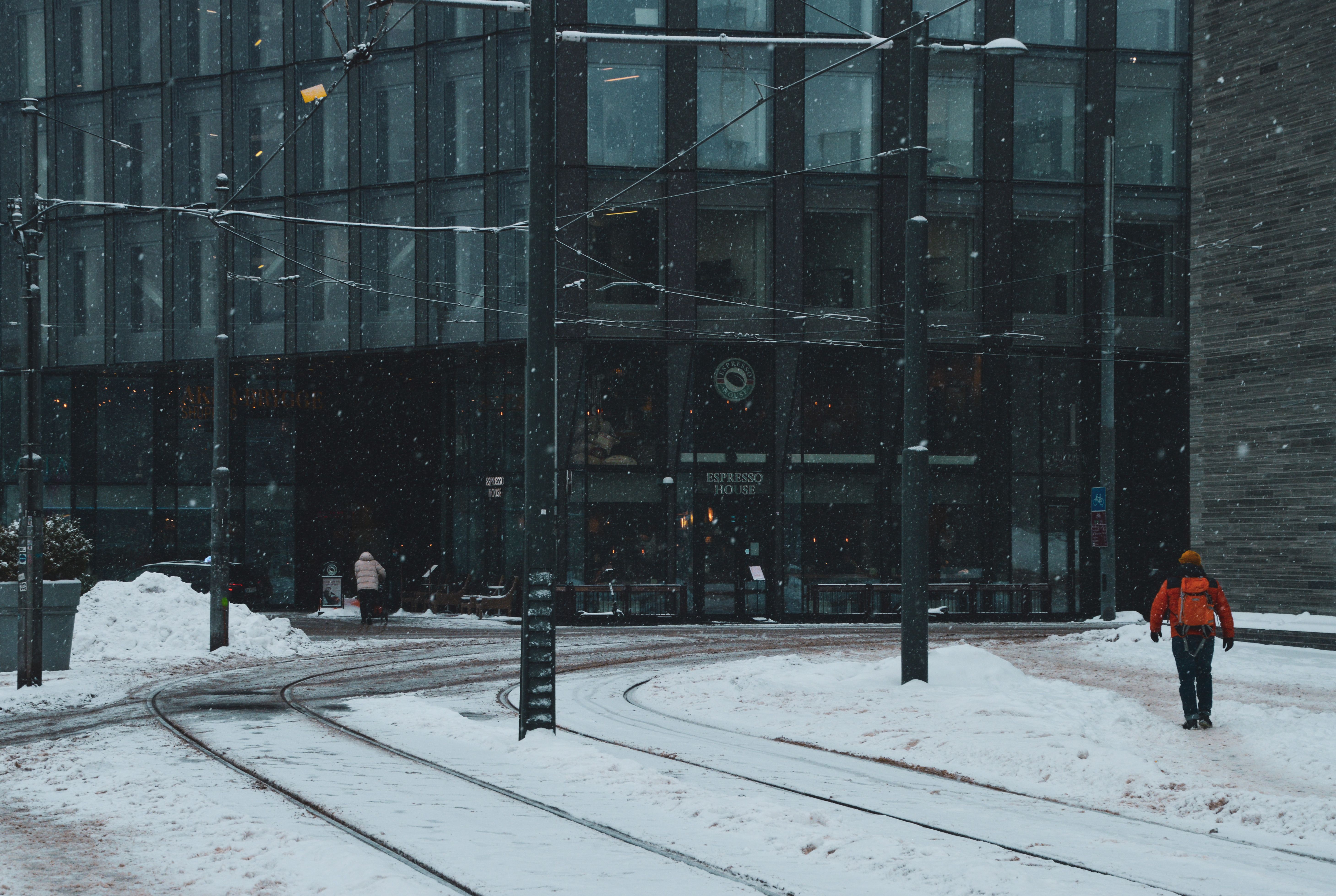 A snowy city street scene with modern buildings and tram tracks, capturing winter urban ambiance.
