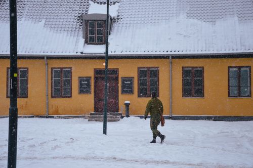Free A person in a green jacket walks past a yellow building on a snowy winter day. Stock Photo