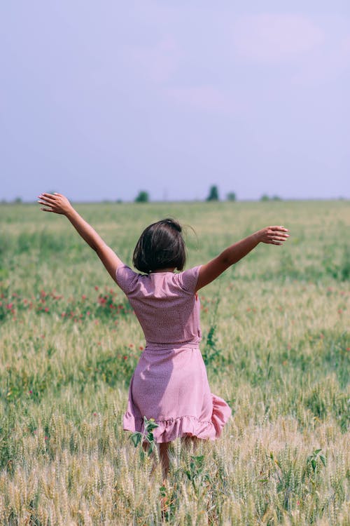 Woman in Pink Dress Standing on Green Grass Field