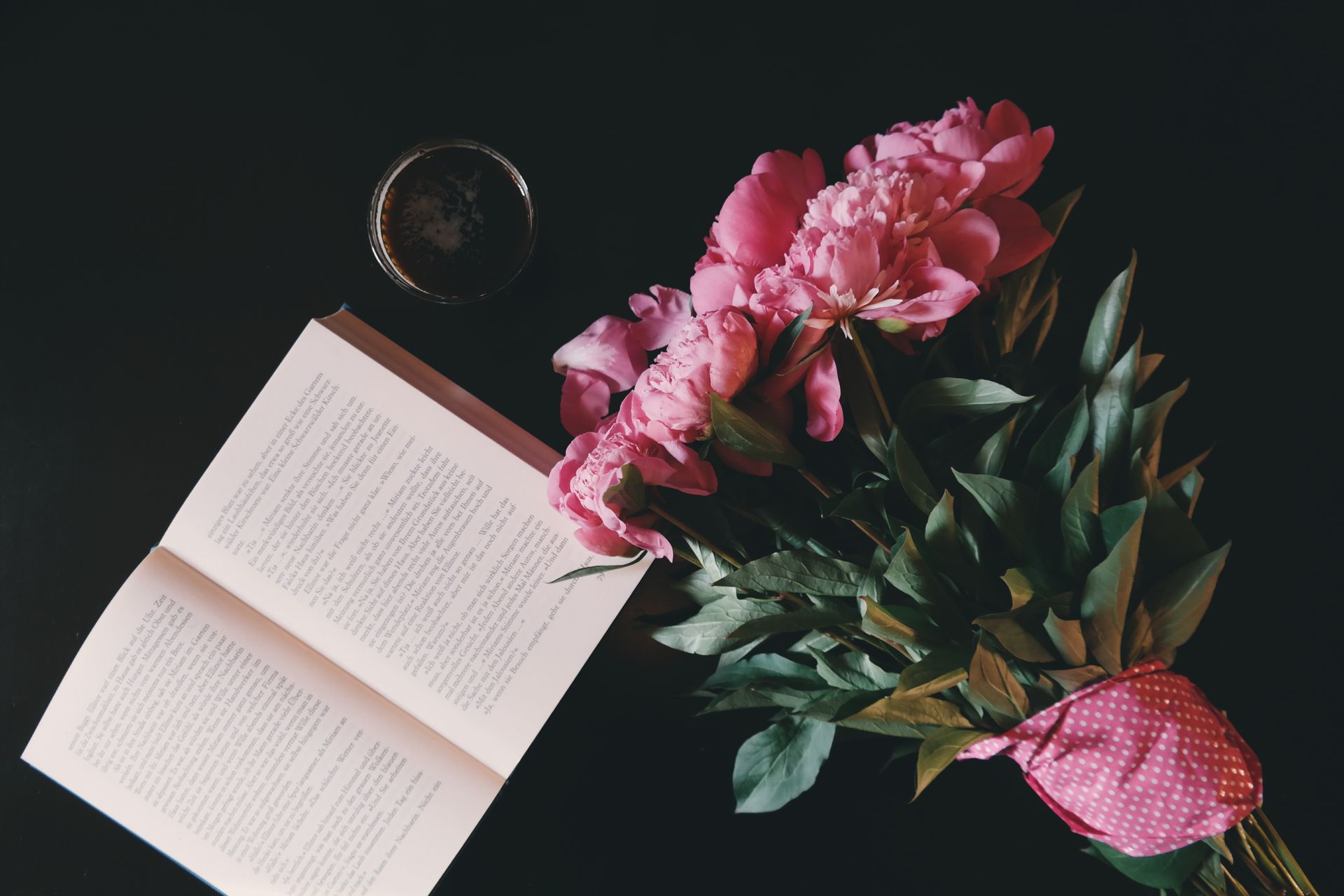 Aesthetic arrangement of pink peonies and an open book, capturing a cozy reading atmosphere.