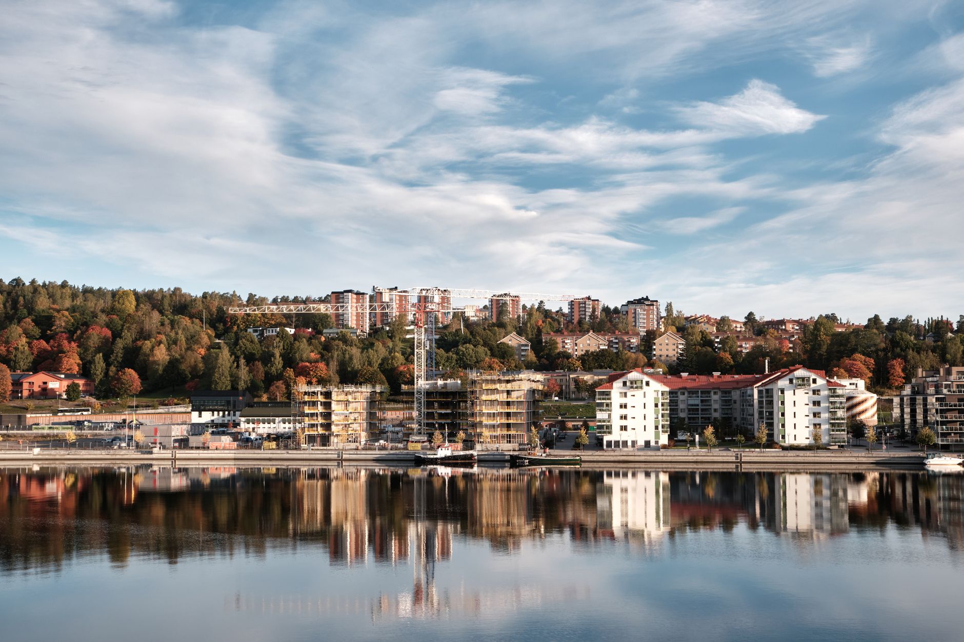 A picturesque urban lakeside view with buildings reflecting in water during autumn.