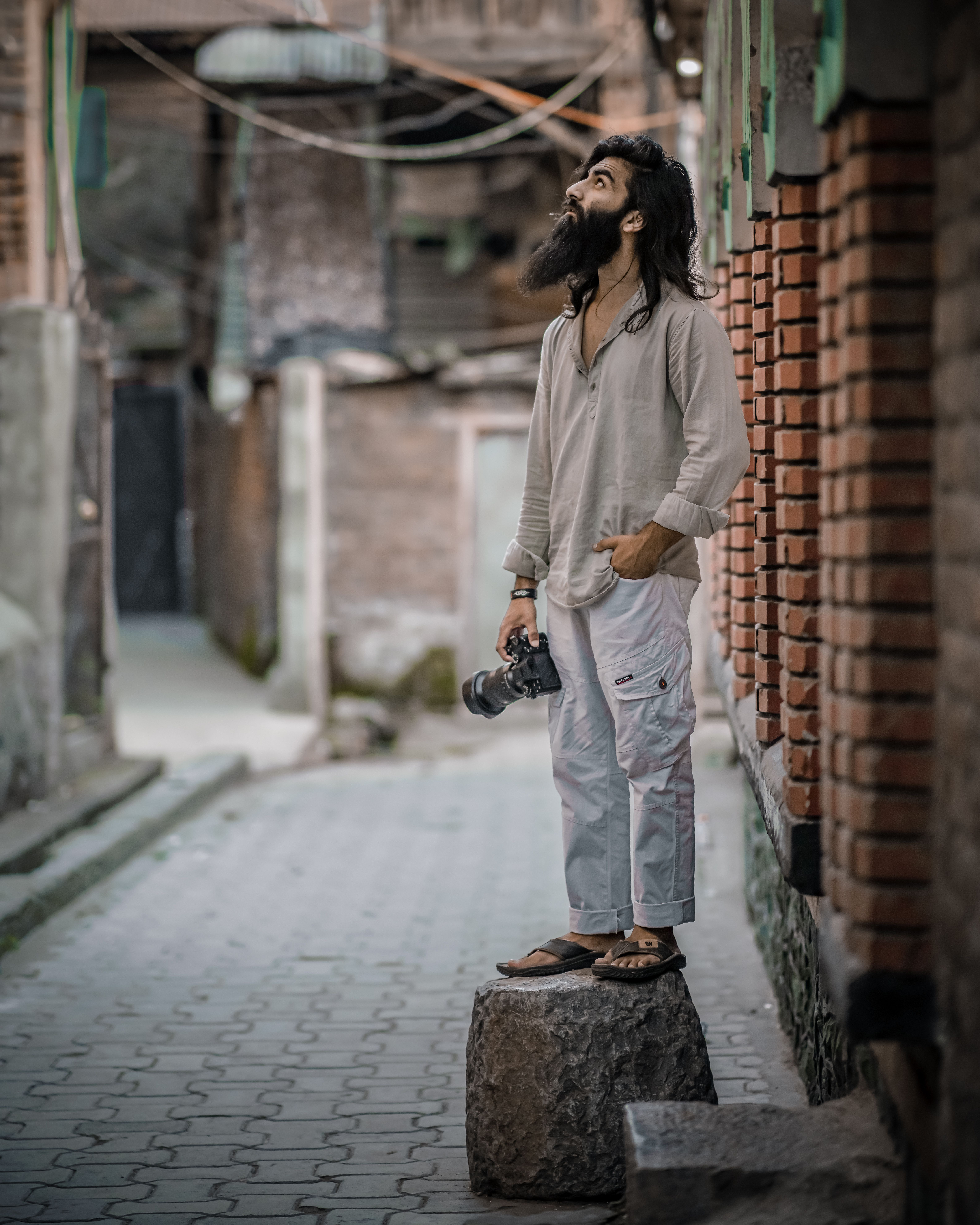 Bearded photographer standing on rock, exploring urban setting.
