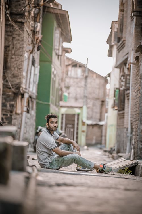 Free A man sits in a narrow urban alleyway, looking thoughtfully at the camera. Stock Photo