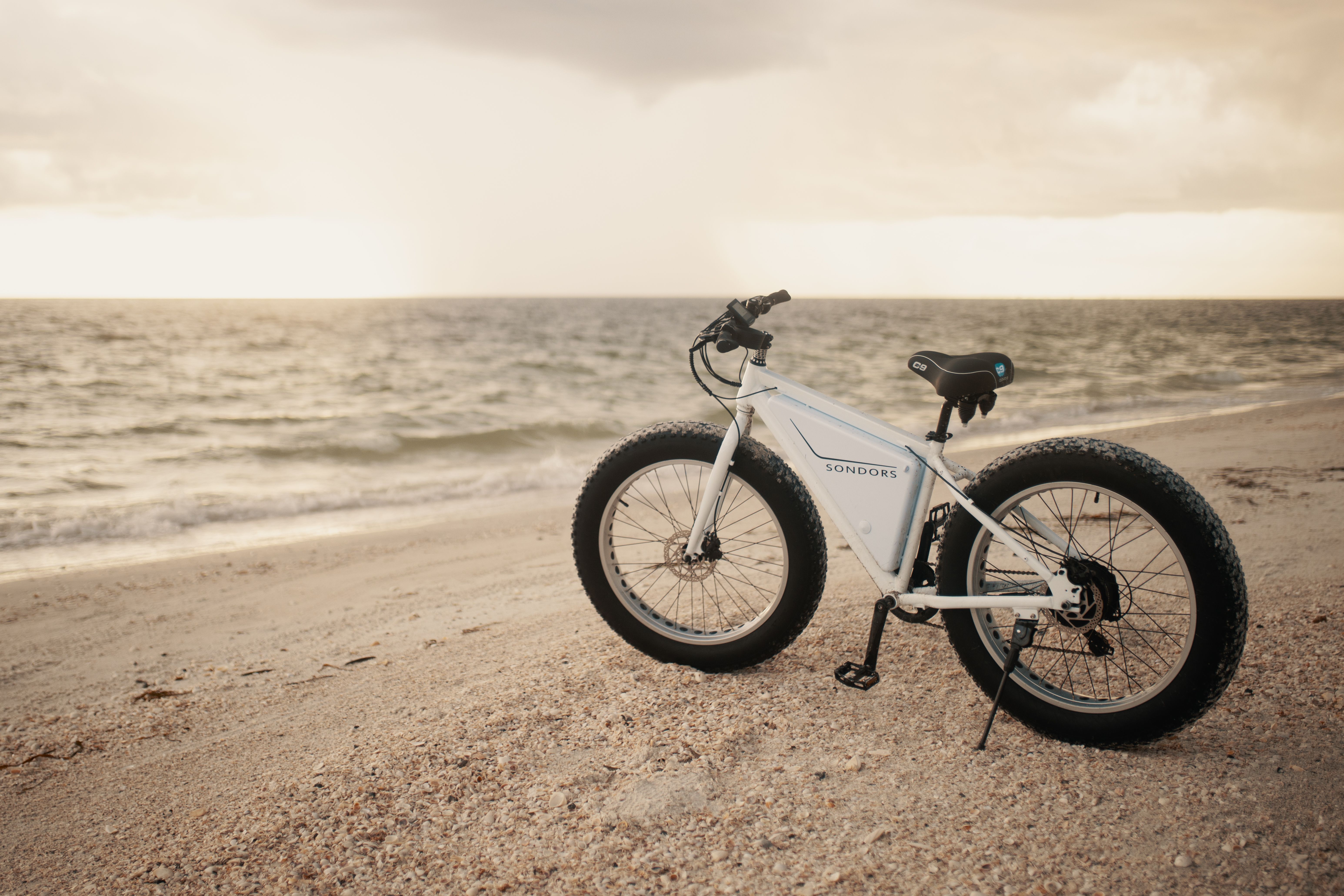 White fat tire bike on a serene beach with ocean waves at sunset.
