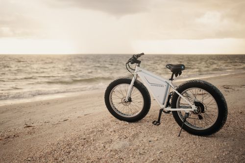 Free White fat tire bike on a serene beach with ocean waves at sunset. Stock Photo