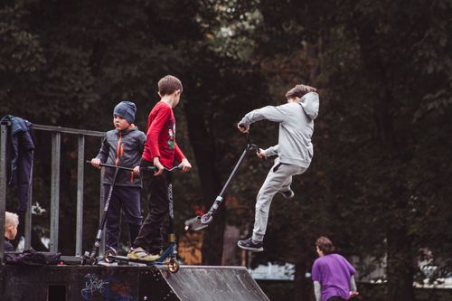 Free Young boys enjoying and performing tricks on kick scooters at an outdoor skate park. Stock Photo