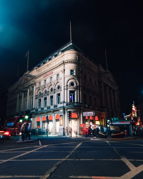 Free Night view of a classic London building with vibrant street lights and bustling activity. Stock Photo
