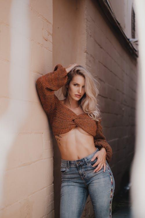 A Woman Wearing Crop Top Top and Denim Jeans Leaning on the Concrete Wall