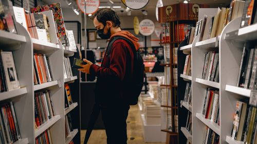 Free Person wearing mask browsing a bookshelf in a modern bookstore during pandemic. Stock Photo