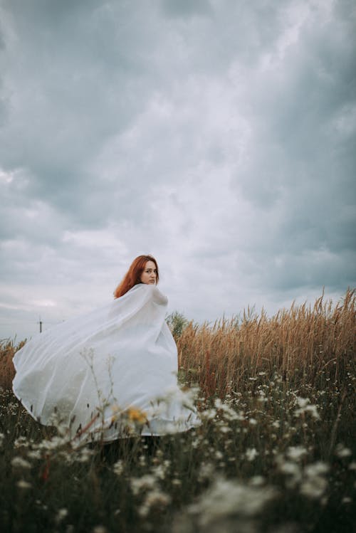 Free A Woman in White Dress Standing on the Grass Field Stock Photo