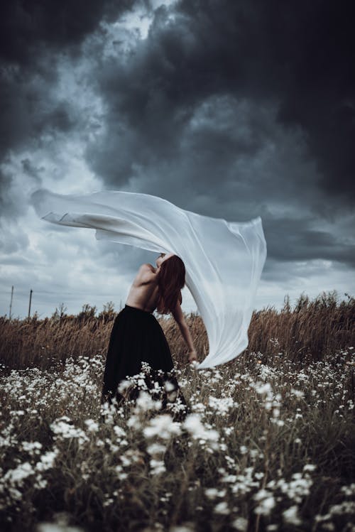 Woman in Black Skirt Holding a White Fabric While Standing on the Grass Field