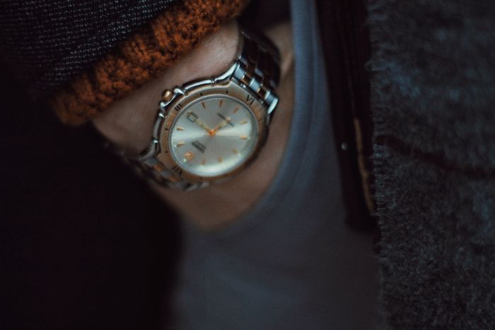 Steel wristwatch peeking from a knit sleeve in low light — photo by Kurchakto on Pexels