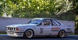 一辆品牌突出的老式赛车停在户外，周围绿化郁郁葱葱