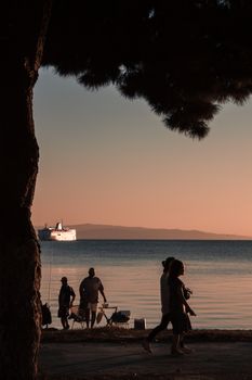 Relaxing evening beach scene with silhouettes and a distant boat on calm water.