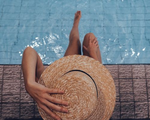 Free Person sitting poolside with a straw hat on a sunny day, enjoying leisure time. Stock Photo