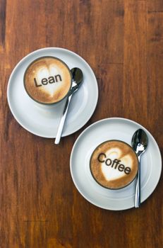 Two cappuccinos on wooden surface with unique latte art, spoons beside. Perfect for coffee enthusiasts.