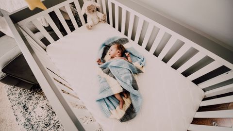 A peaceful baby wrapped in a blanket sleeps in a cozy crib, creating a serene nursery atmosphere.