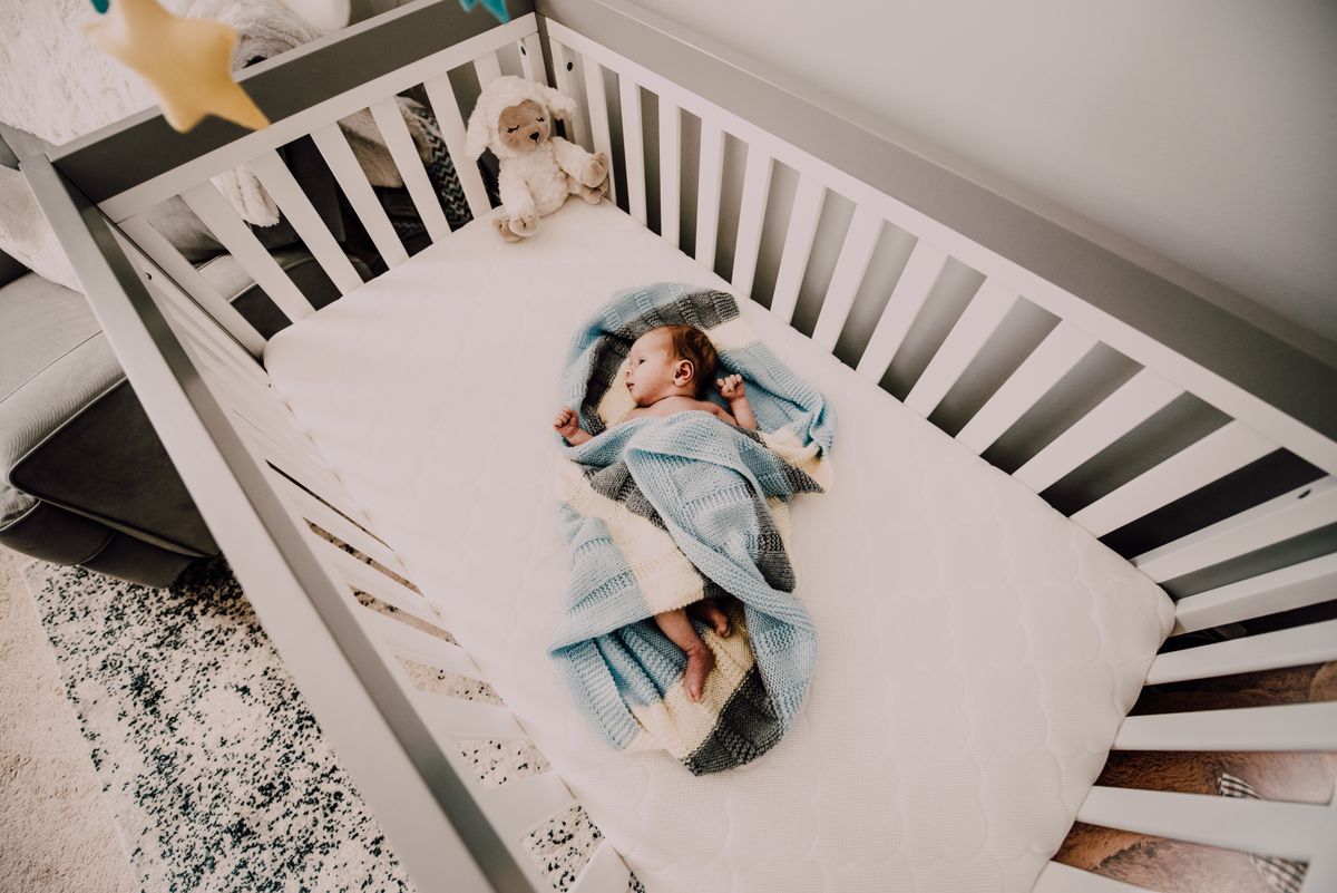 Baby sleeping on its own sleep surface in a blue blanket