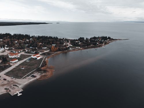 Free A serene aerial view of a coastal village with forests, coastline, and calm sea. Stock Photo