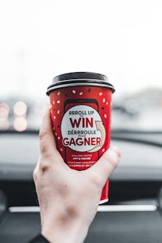 Close-up of a hand holding a red coffee cup with promotional text inside a car.