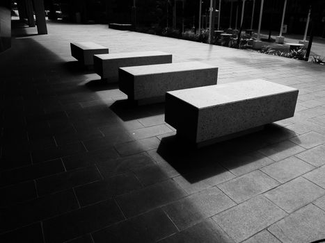 Concrete benches casting shadows on a tiled floor in an urban setting.