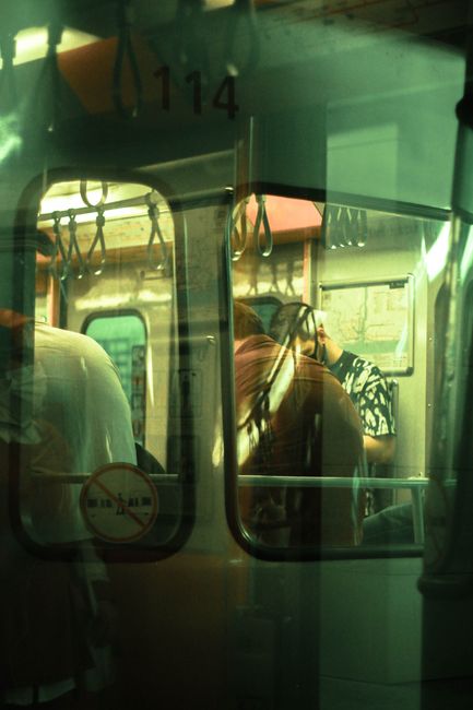 Passengers standing inside a subway train seen through a window, depicting urban transportation life.