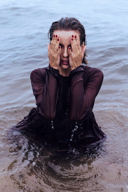 Woman posing in sea with hands on face