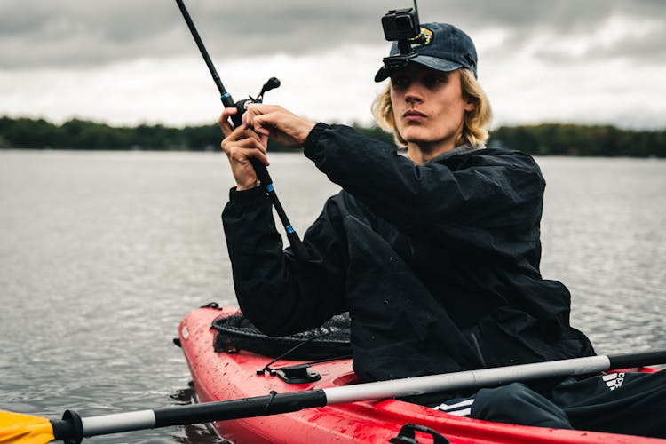 A Man In Black Jacket Riding A Kayak While Holding A Fishing Rod