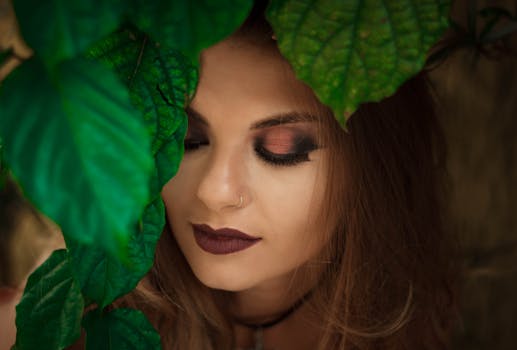 A beautiful portrait of a woman with rich eye makeup surrounded by vibrant green leaves.