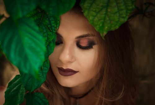 Free A beautiful portrait of a woman with rich eye makeup surrounded by vibrant green leaves. Stock Photo