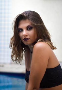 一位黑发女子浓妆艳抹，在室内泳池边摆姿势的肖像十分迷人