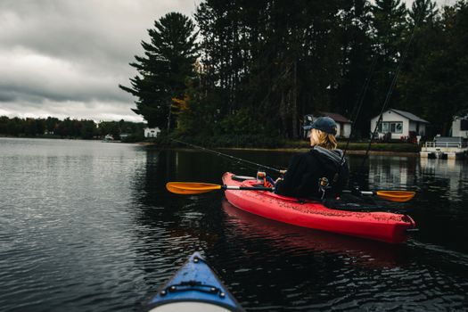 A person in a red kayak fishing on a serene lake under a cloudy sky.