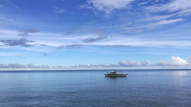 A fishing boat floats on the tranquil ocean under a vibrant blue sky in Brooke's Point, Philippines.