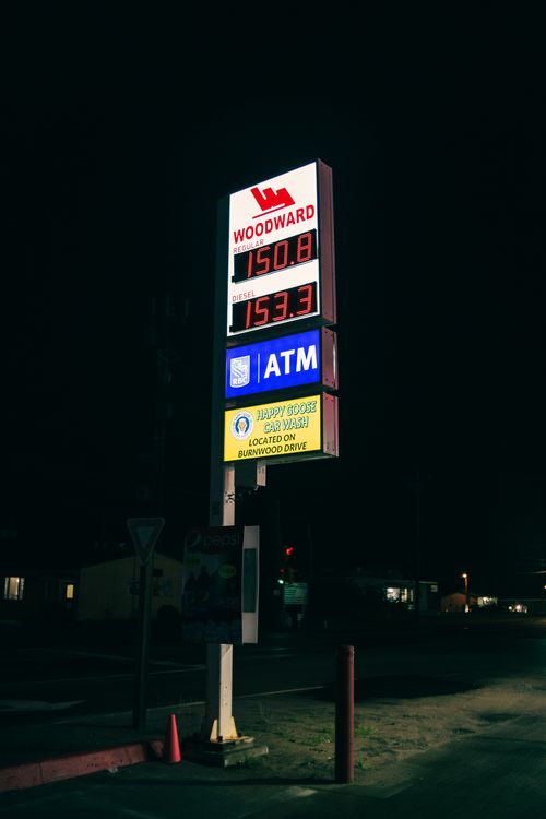 Free Gas station sign illuminated at night displaying fuel prices and ATM availability. Stock Photo