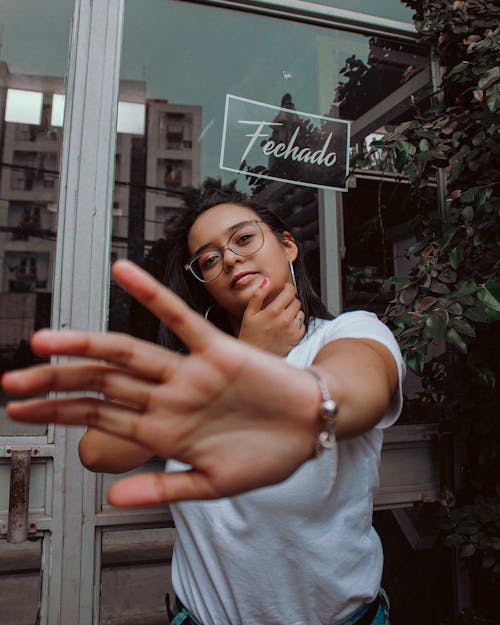 A Woman in Eyeglasses Standing Near Glass Wall while Looking at the Camera