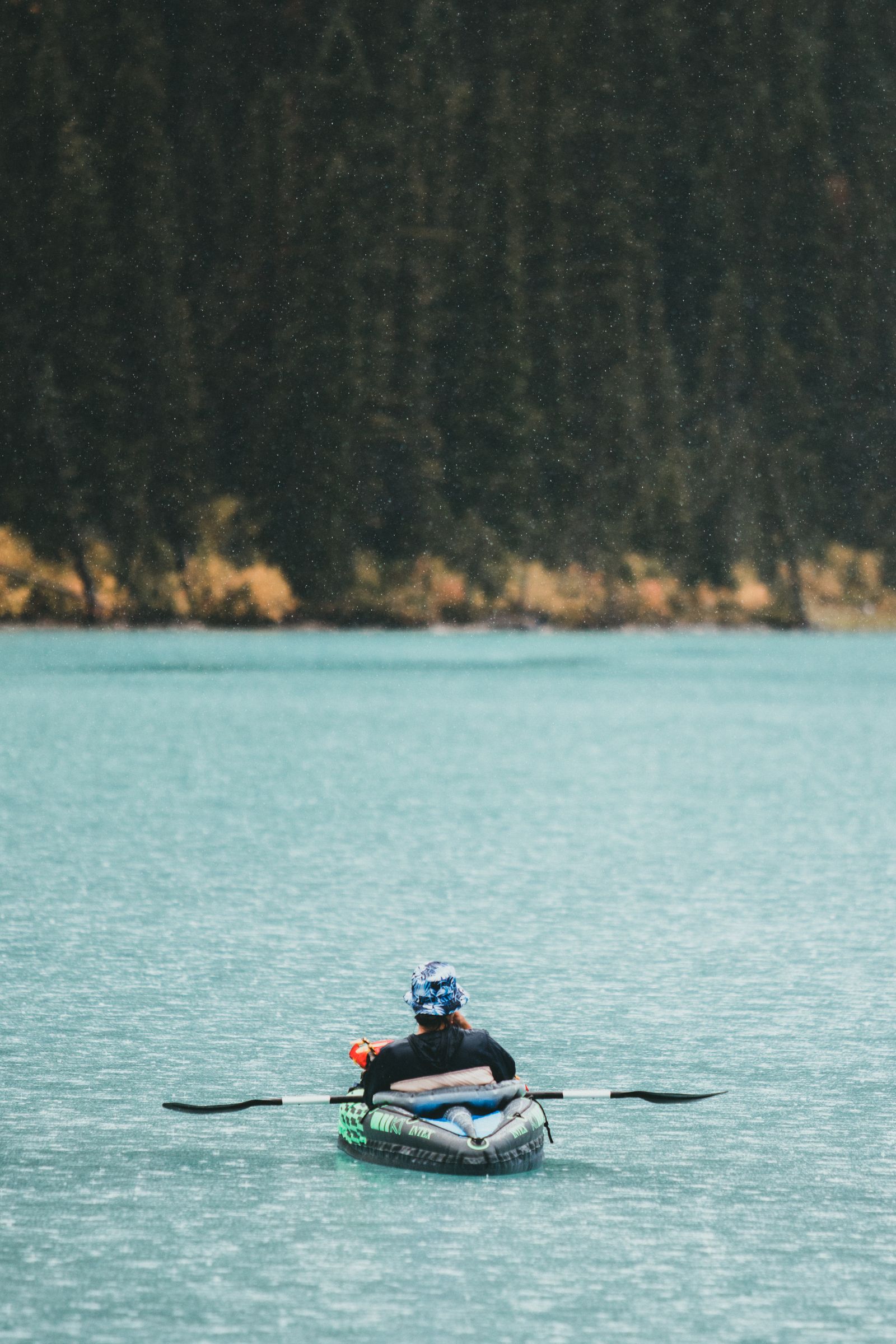 A person kayaking on a calm lake, paddle in hand, surrounded by water and trees