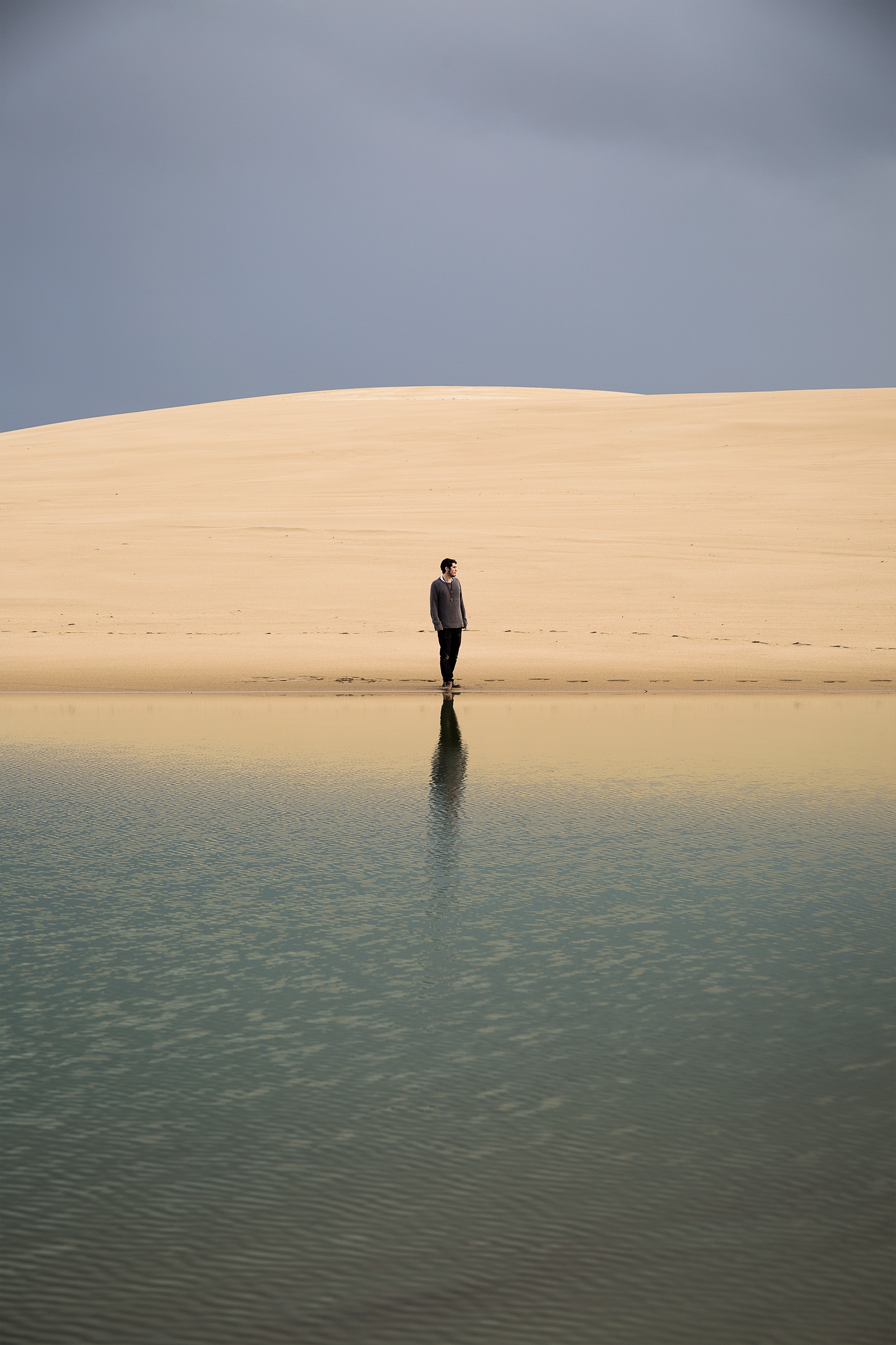 A lone person stands on a serene beach near Oregon's sand dunes.