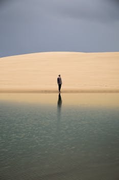 A lone person stands on a serene beach near Oregon's sand dunes.