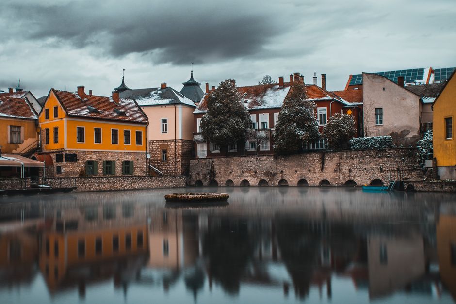 Picturesque view of Tapolca Hungary reflecting on tranquil waters under cloudy skies.
