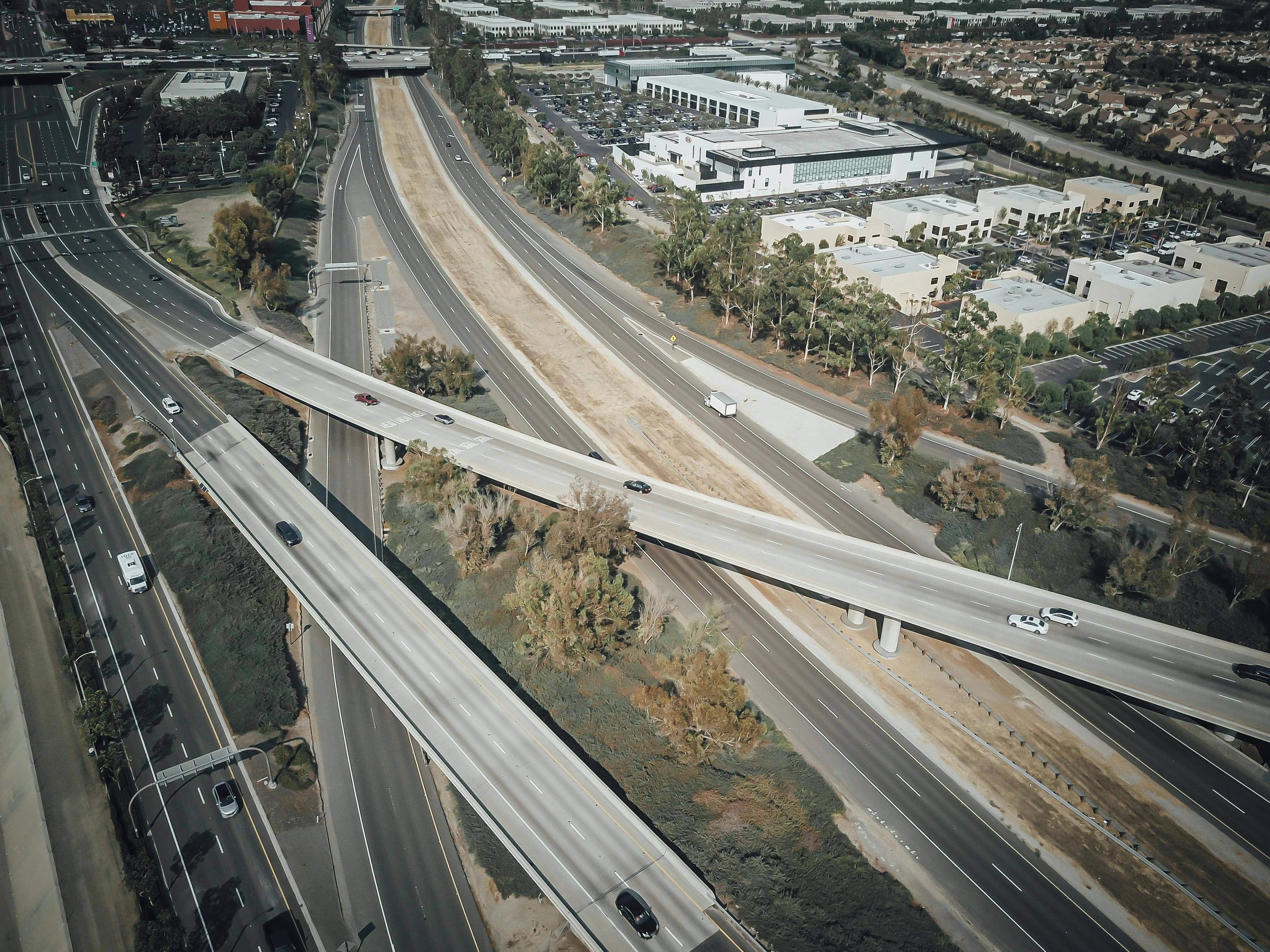 Drone shot of an urban highway interchange with moving vehicles and surrounding cityscape.