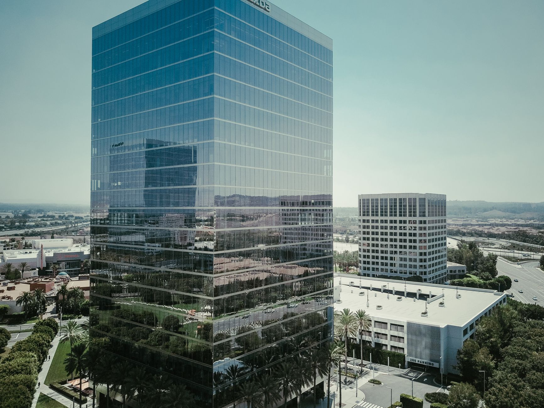Tall glass skyscraper reflecting the cityscape in a modern urban setting under a clear sky.