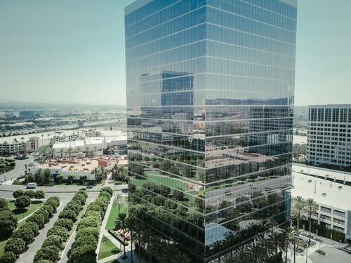 Free High-rise building with glass facade reflecting city streets and greenery in daytime. Stock Photo
