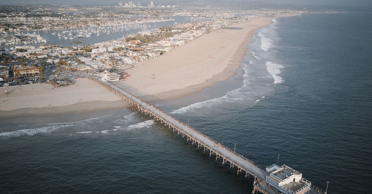 A stunning aerial shot of Newport Beach Pier extending into the ocean with the coastline and city in the background.