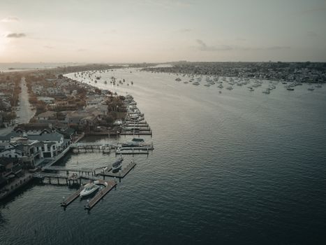 Drone shot of coastal marina with yachts and residential buildings under a moody sky.