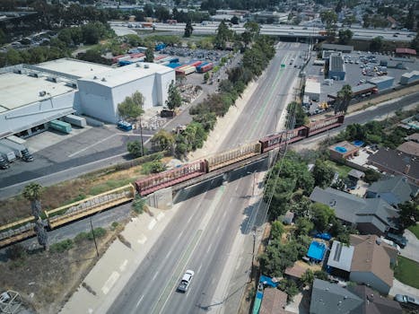 Aerial view of a cargo train crossing over a busy expressway in an urban area.