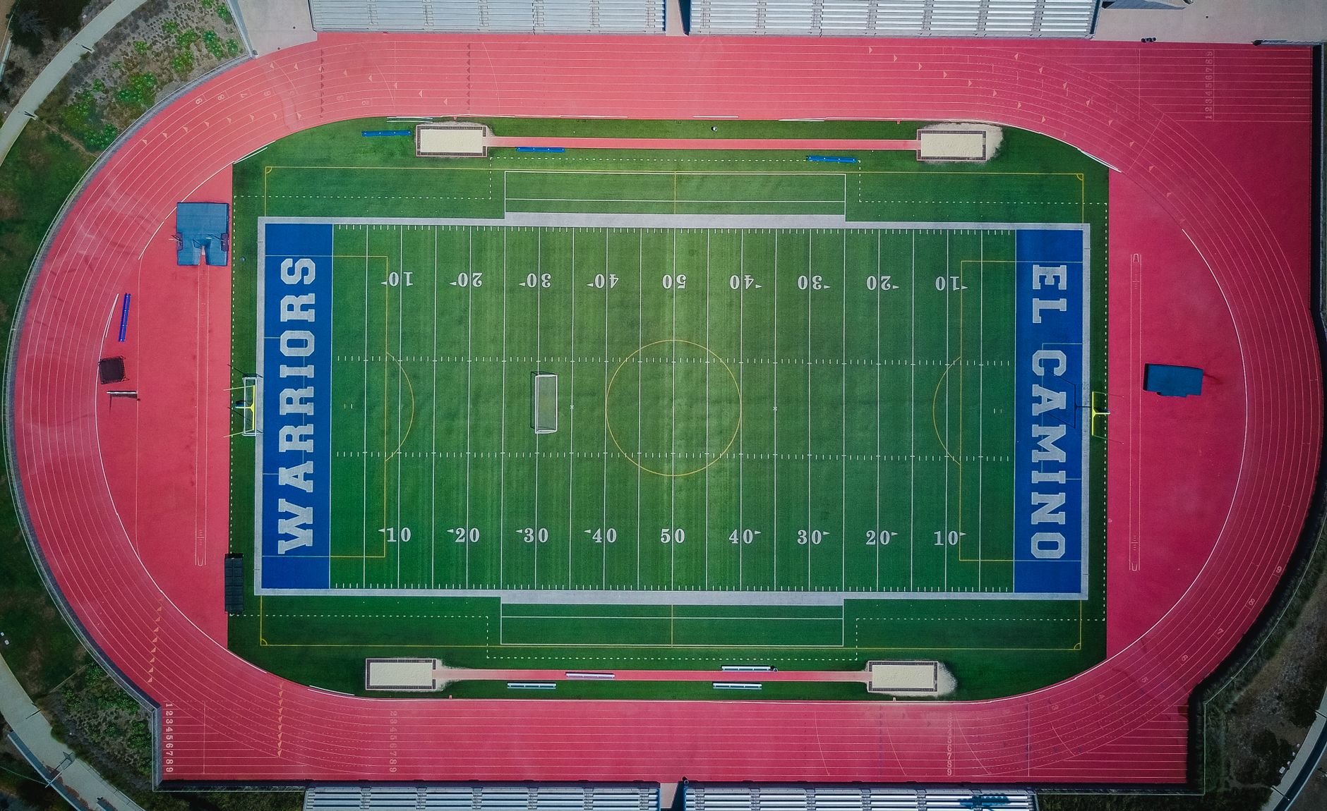 Top-down aerial view of El Camino football stadium with vibrant green field and red track.