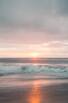 Calm ocean waves reflect a stunning pastel sunset, perfect for tranquil nature scenes.