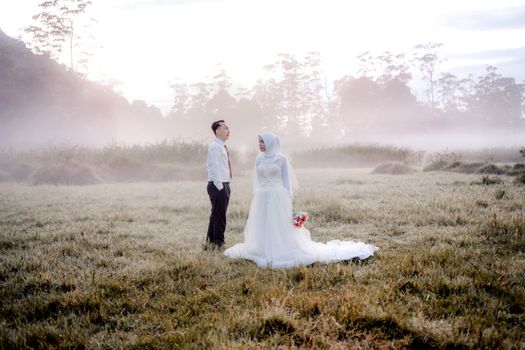 Elegant outdoor prewedding photo of a couple in a misty grassland in Indonesia. - Fotografer Sidoarjo