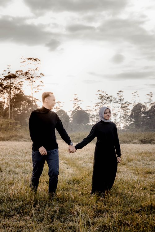 Free An Asian couple in love walks hand in hand across a scenic field at sunset in Indonesia. Stock Photo
